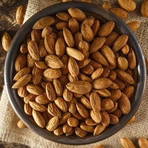 Raw whole Kashmiri almonds in a dark bowl on jute